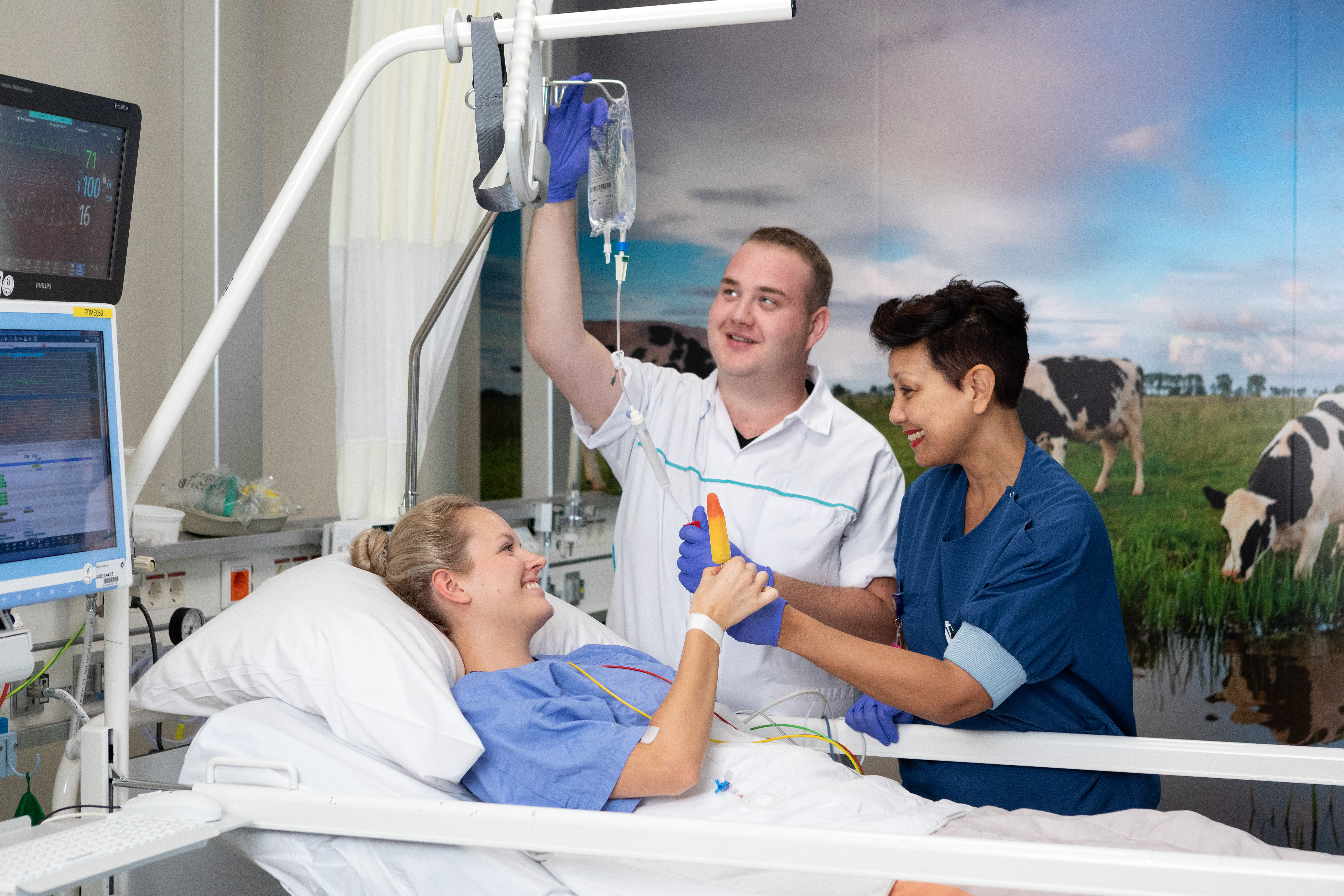 Patiënt in bed krijgt ijsje van twee verpleegkundigen.