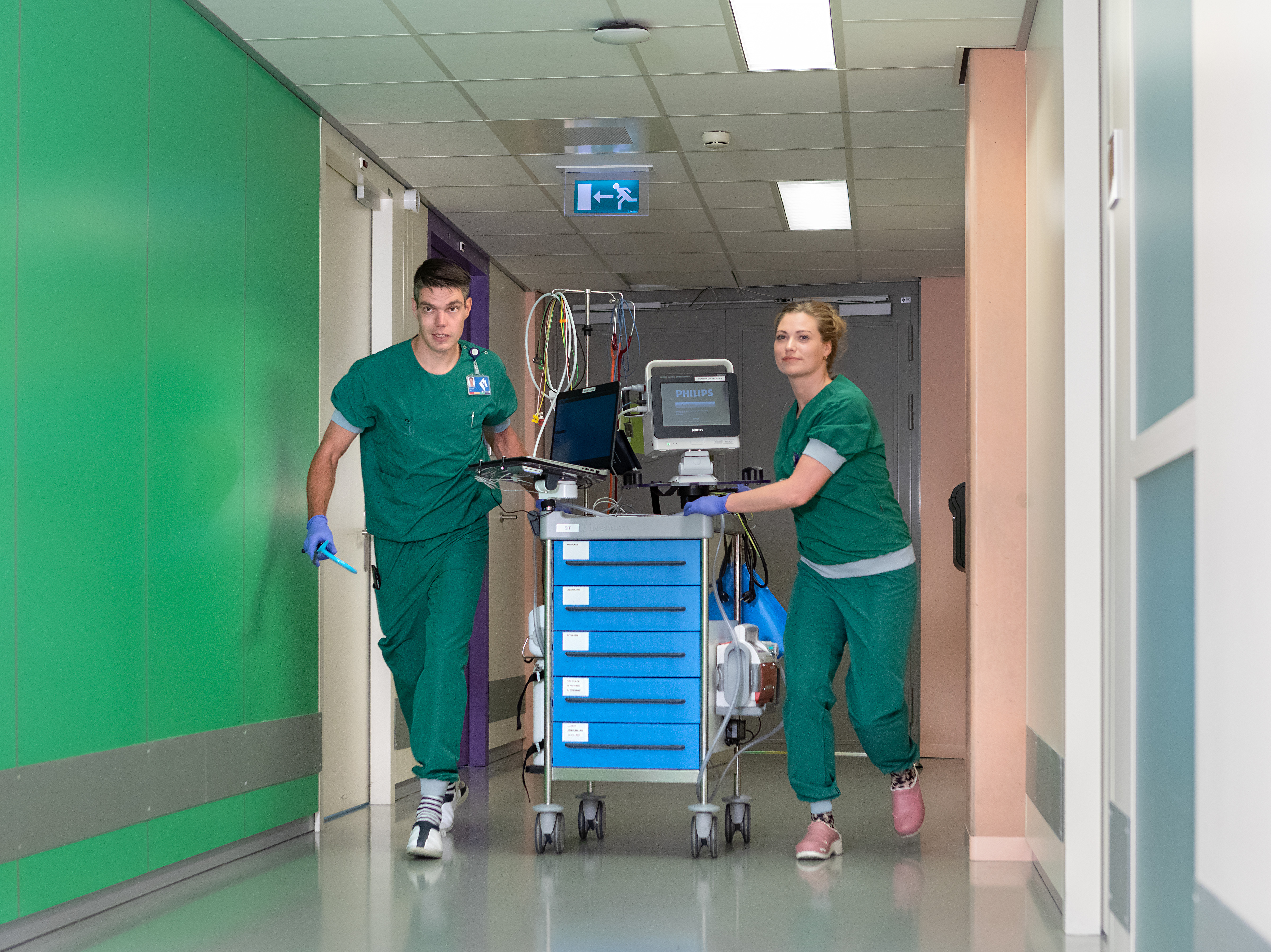 Twee verpleegkundigen met medisch apparatuur in de gang van de Intensive Care.